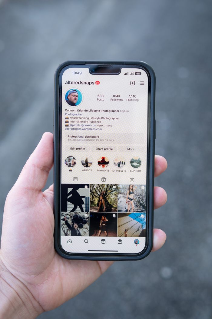 Close-up of a smartphone showing a social media profile, held by a hand outdoors.